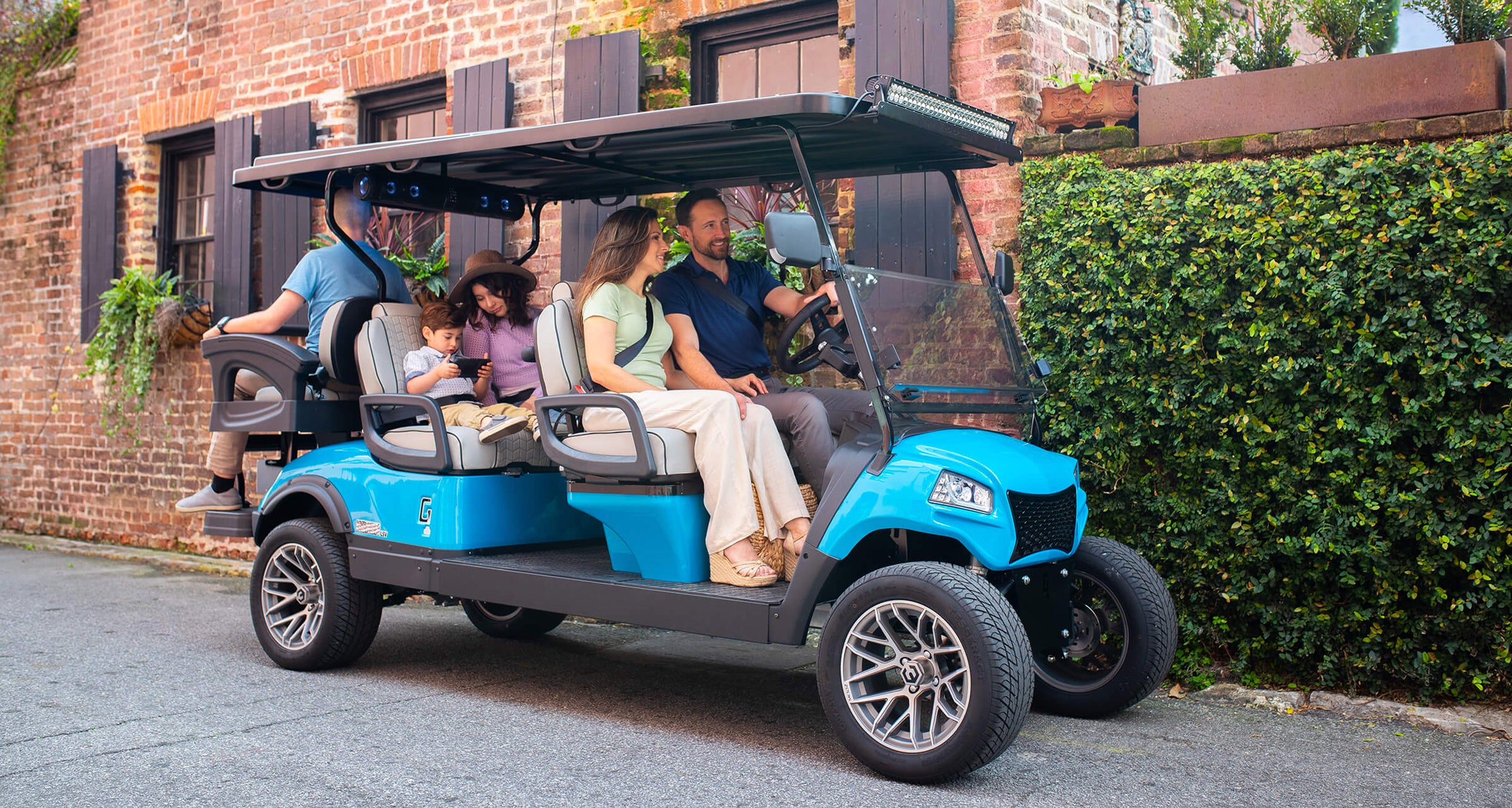 Family in a blue golf cart parked on a street next to a brick building.